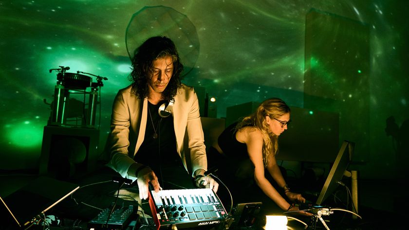 two dj's twirl knobs on electronic devices in front of swirling colored projects on art gallery walls behind them