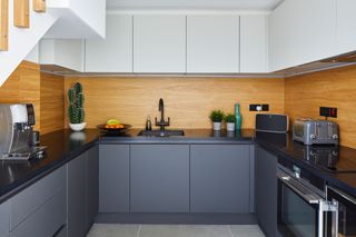 u shaped kitchen with wood backplash, charcoal grey cabinets and white cabinets in a modern home