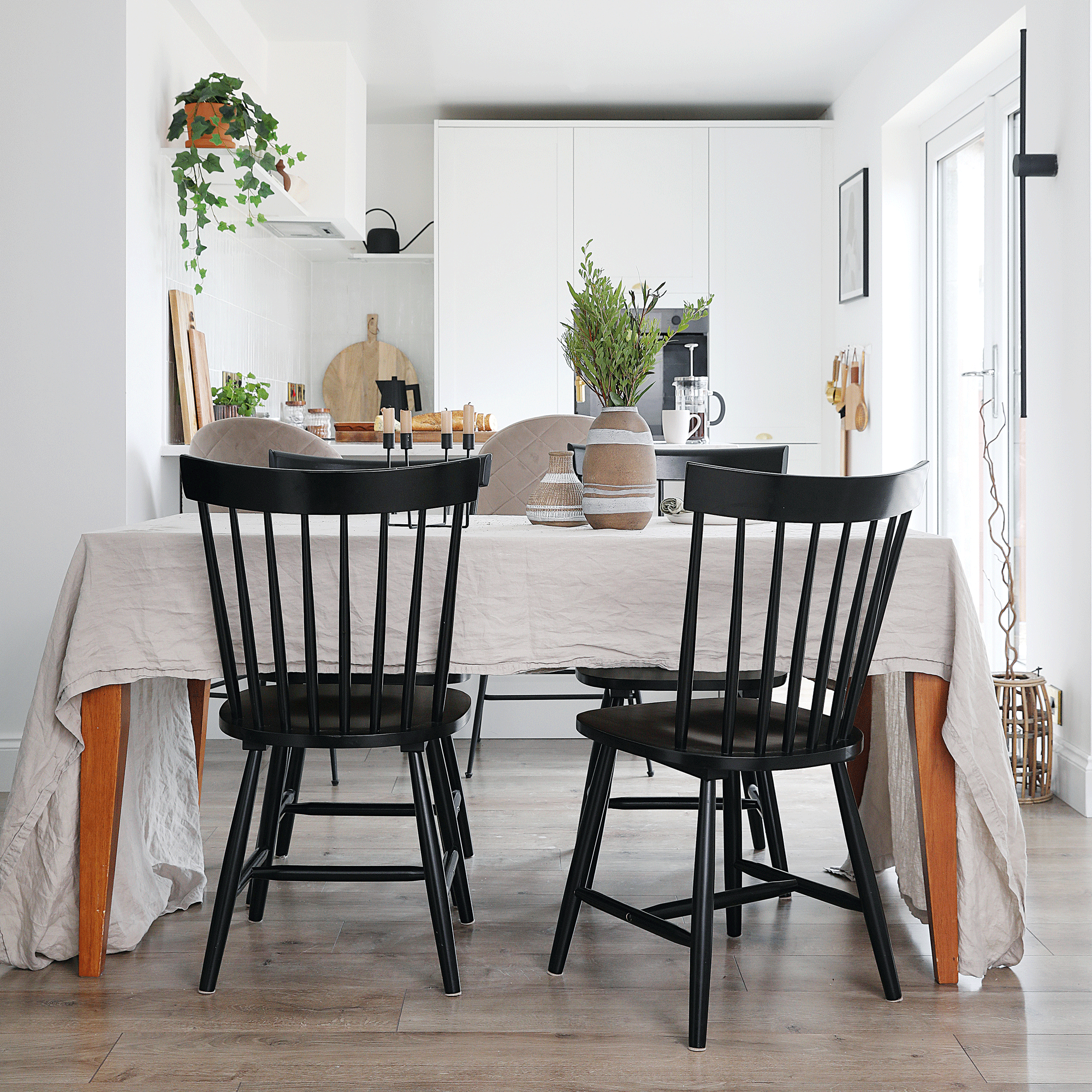 an open plan kitchen dining area with a black table and dining table and chairs covered in a linen tablecloth and a small kitchen with floor to ceiling storage