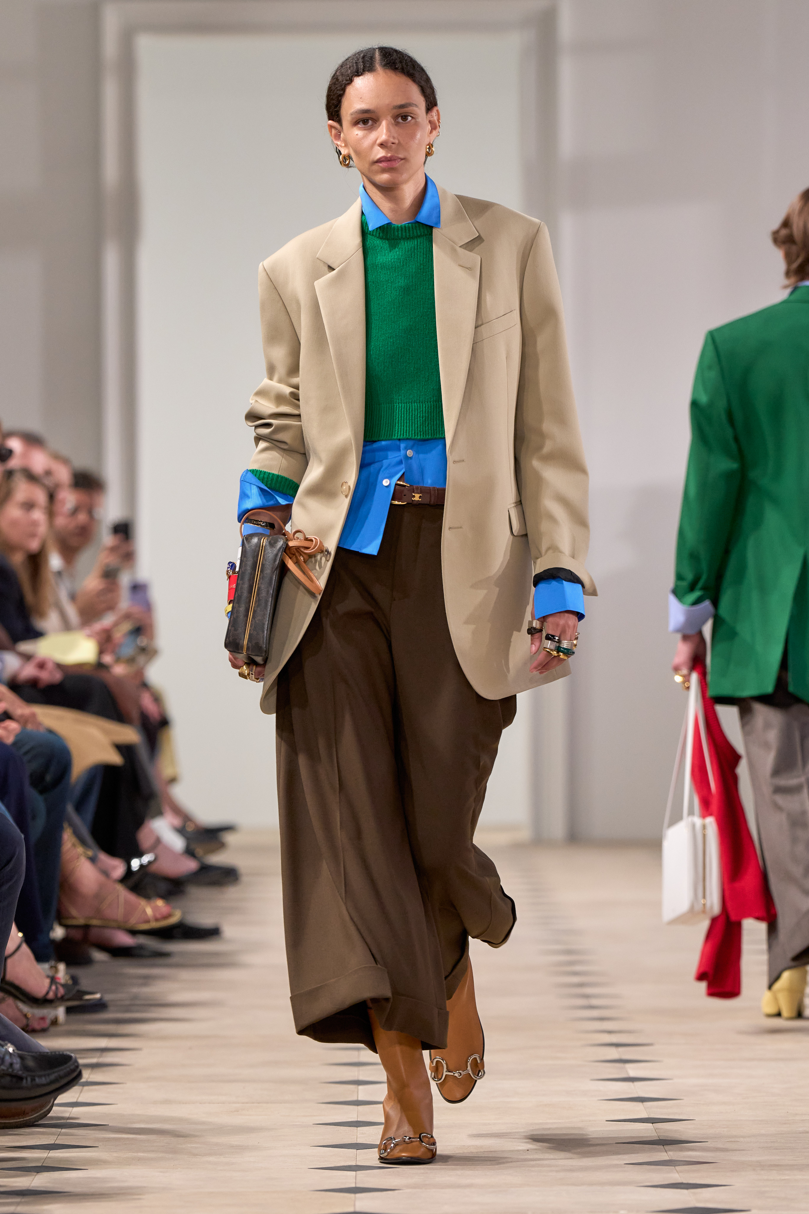 a model walks the Celine runway wearing a blazer with a layered sweater and black pants