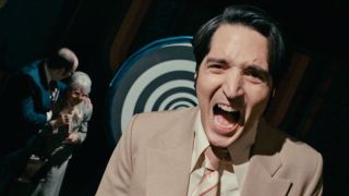 David Dastmalchian laughs maniacally in front of a hypnotic background in Late Night with the Devil