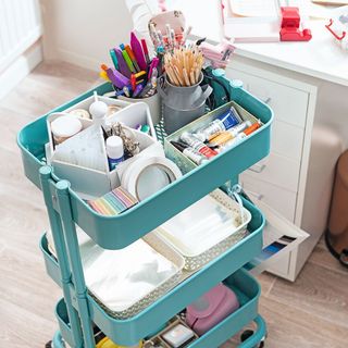 Teal trolley displaying arts and crafts supplies next to white desk