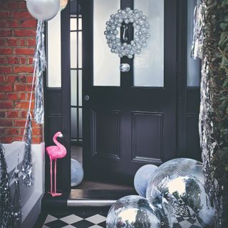 Black front door decorated with a disco ball Christmas wreath, silver balloons and tinsel and oversized disco balls on the tiled chequered floor