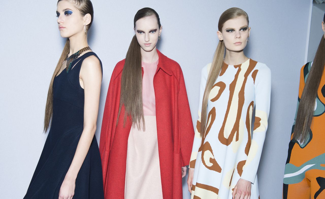 Three women, one in a black dress, one in a red coat, and one in a white and brown dress