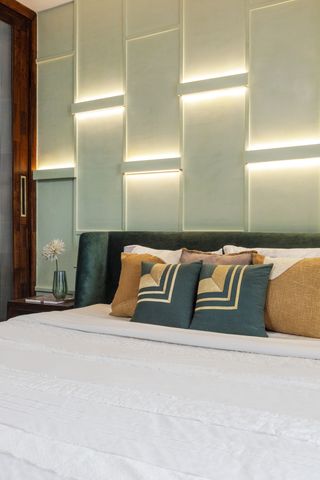 A bedroom with recessed lighting behind the bed
