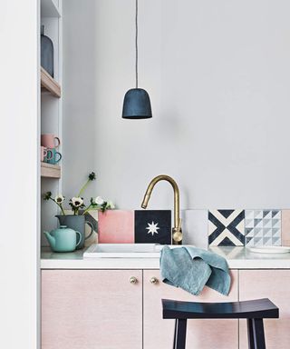 Kitchen with a splashback made from mismatched decorative tiles, kitchen units with a white worktop and a black stool.