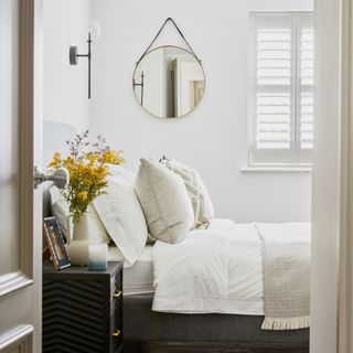 Round hanging mirror with white bedding and cushions above the bed