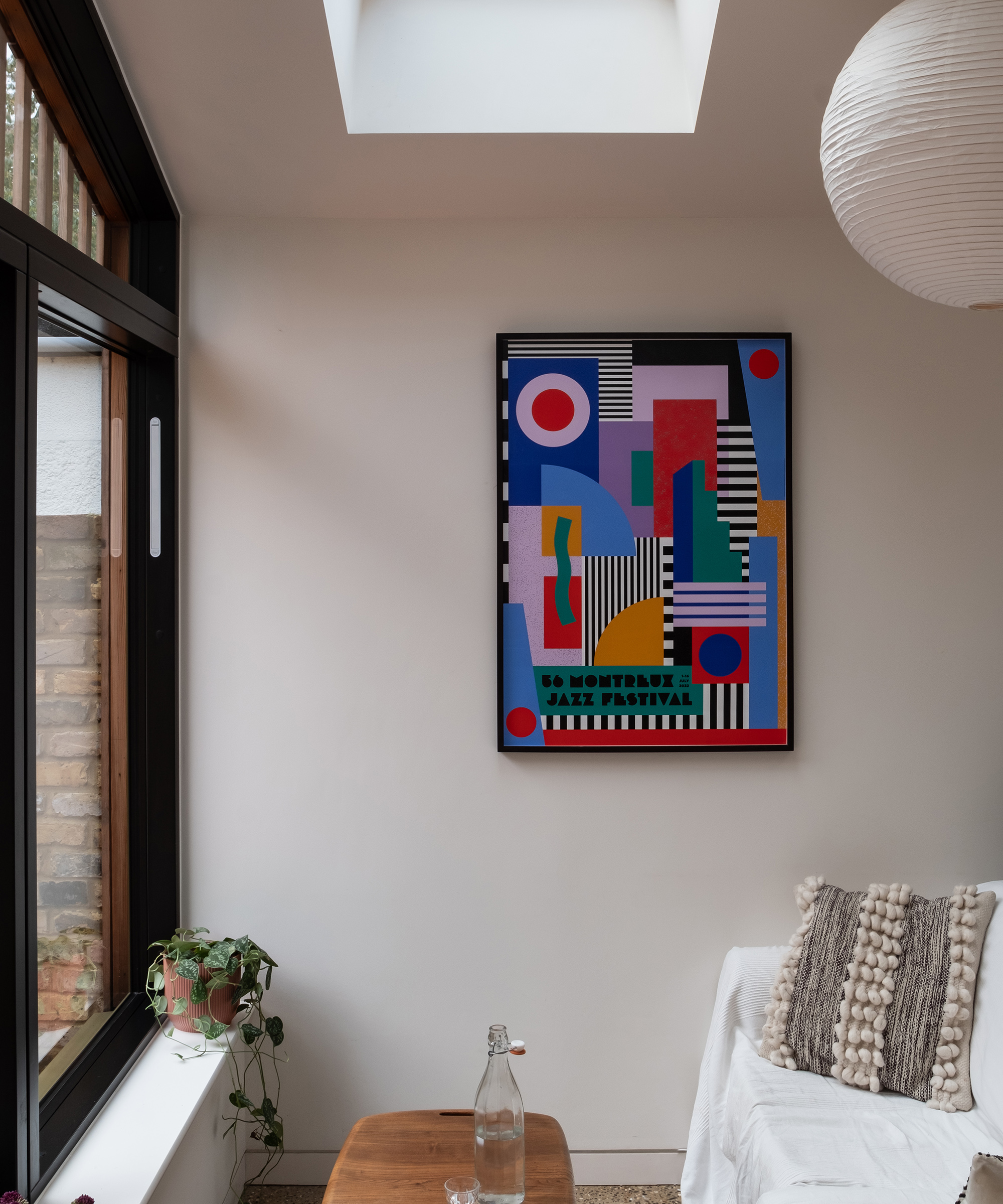 A bold abstract print on a wall in a kitchen extension. There is a sofa which faces a large window looking out to the back garden