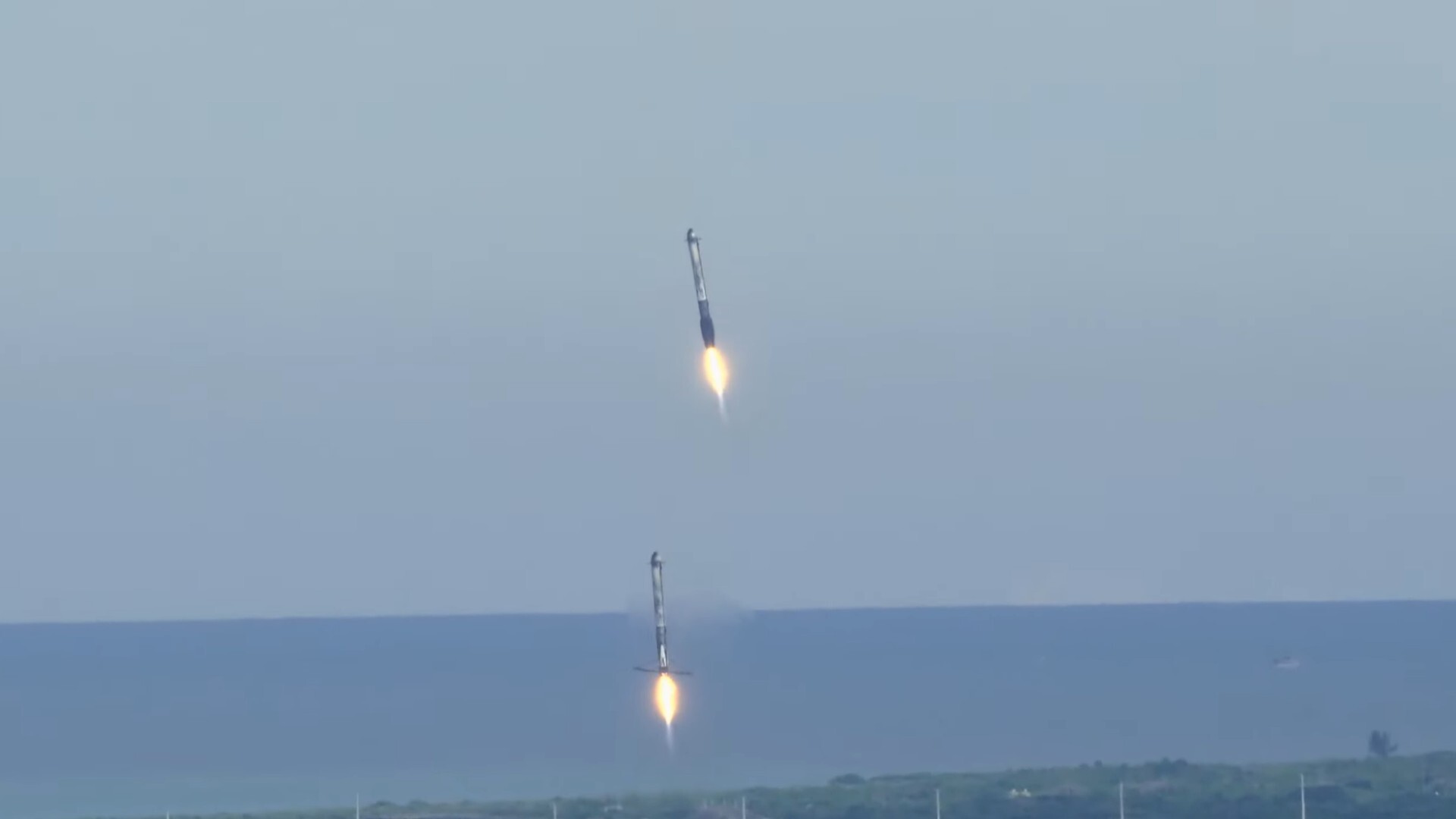 two rockets come down for a landing with the ocean in the background