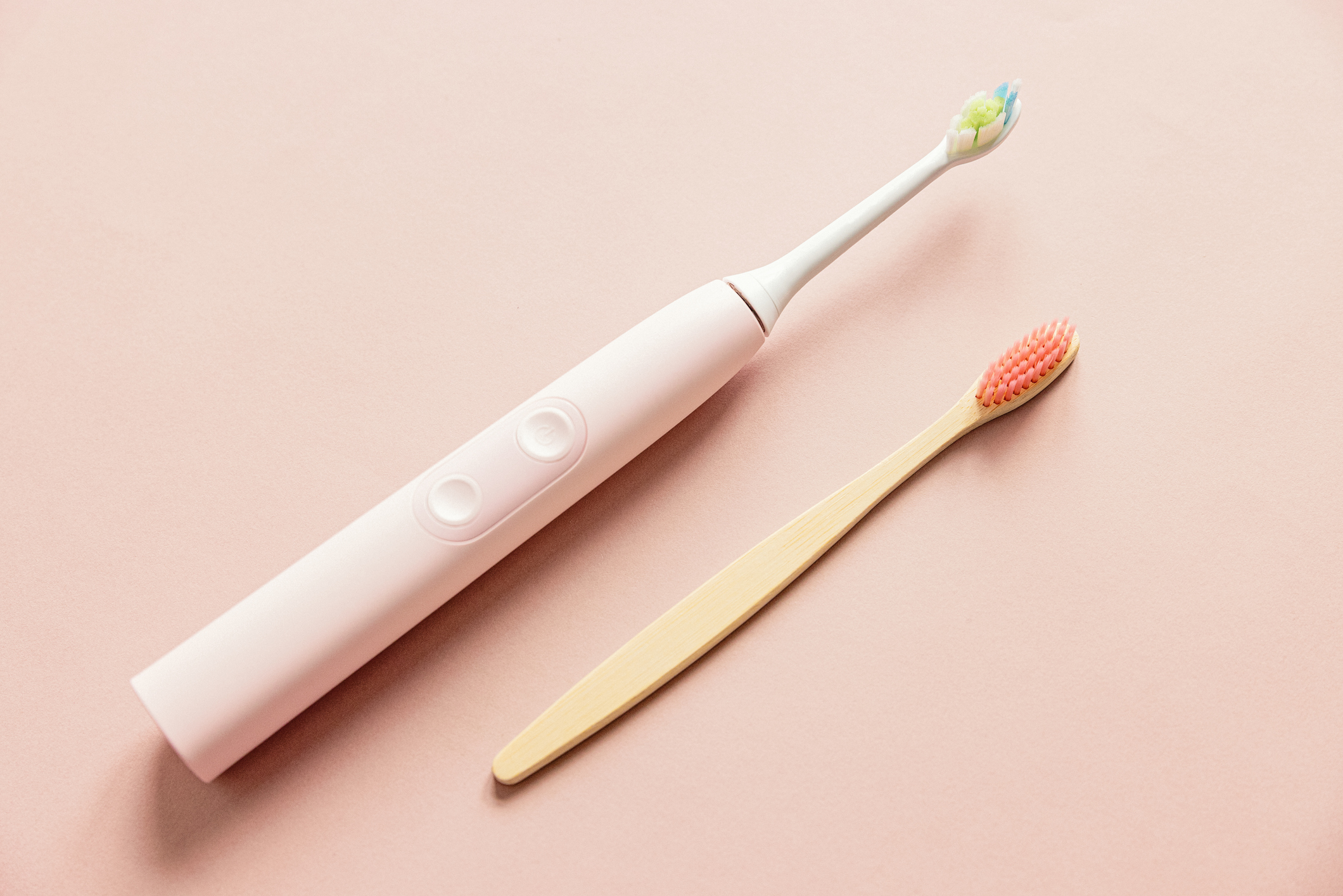 an electric toothbrush next to a manual toothbrush on an orange background