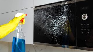 A person spraying cleaning solution onto a microwave