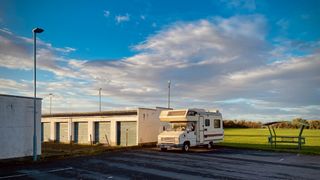 Camper van parked next to a row of garages and a games field with dramatic lighting