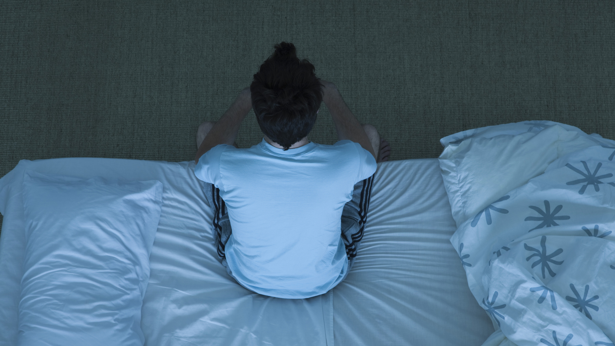 A man with insomnia sits on the edge of his bed during another sleepless night