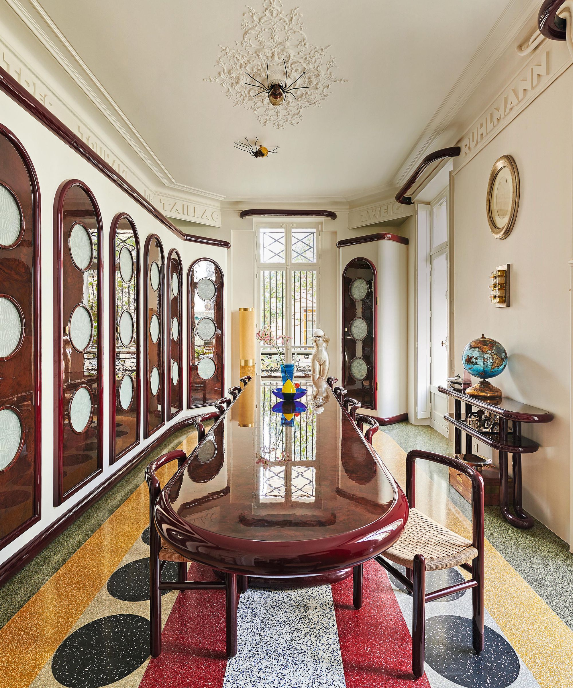 an eclectic colorful dining room with porthole arched doors and a curved red table