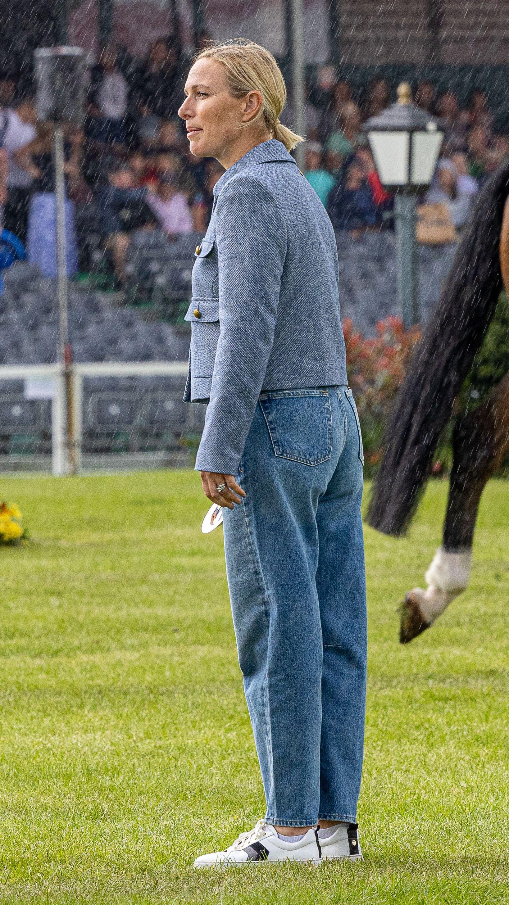 Zara Tindall stands in the rain at the Badminton Horse Trials wearing barrel leg jeans