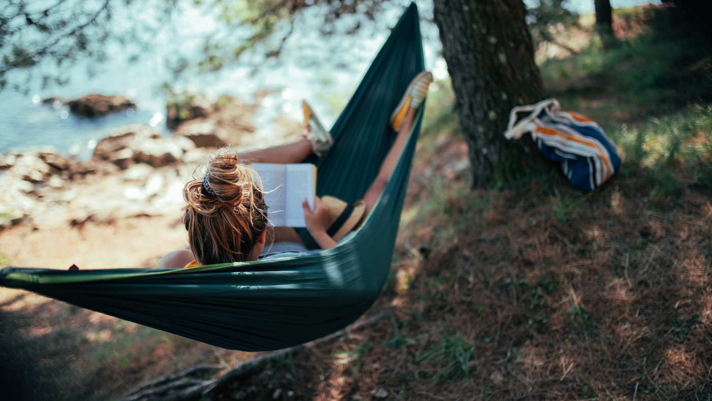 A woman reading in a hammock by a lake