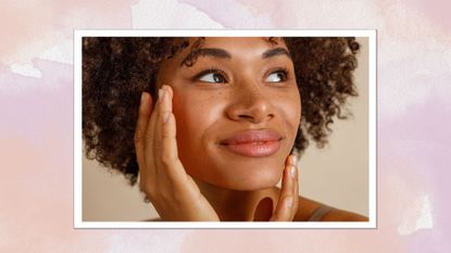A pink watercolour frame containing a close up image of a woman's face, with curly hair and clear skin, touching her cheek and jawline