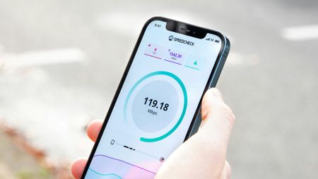 A person holds an iPhone while it is performing a 5G speed test.