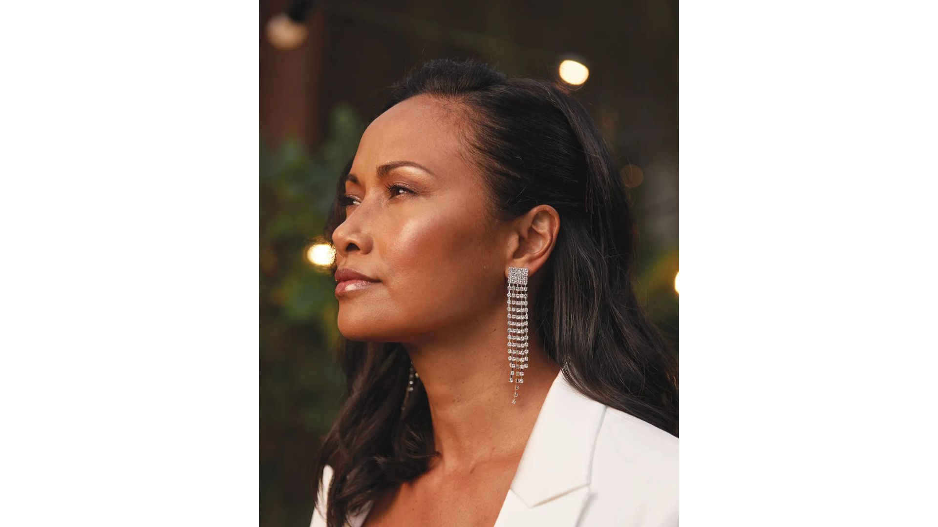 A woman with brown side parted hair and glowing skin wearing a sparkly dangly earring in profile