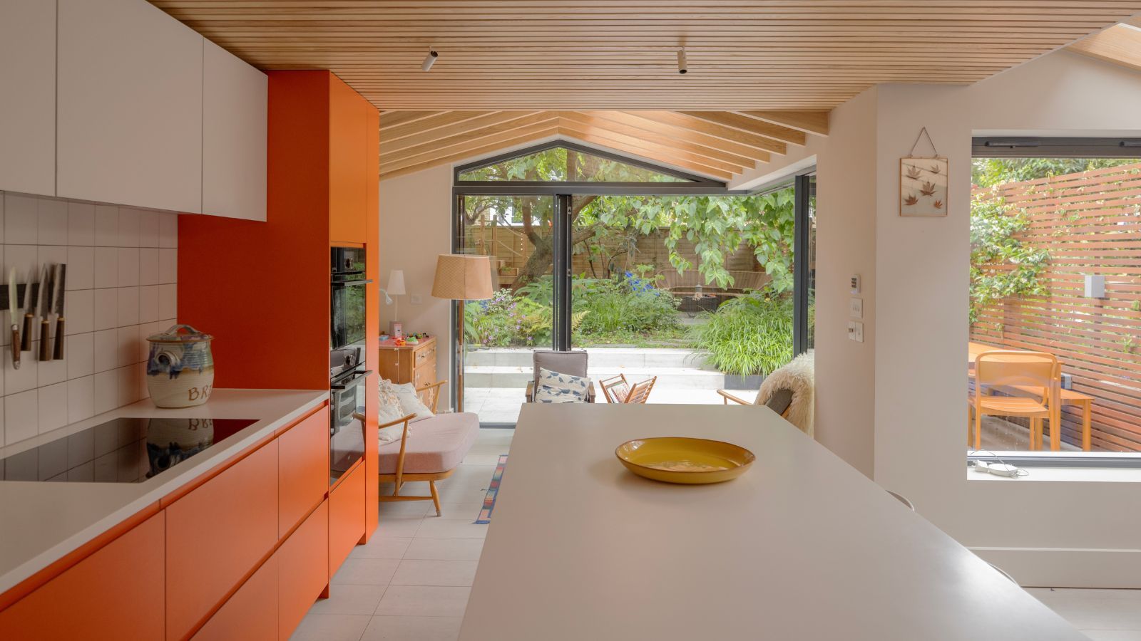 Kitchen with orange cabinets, white countertops, white walls, and wooden ceiling paneling