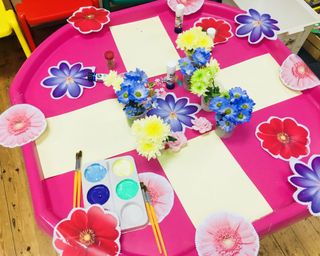 A pink tuff tray with paints and cutouts of flowers