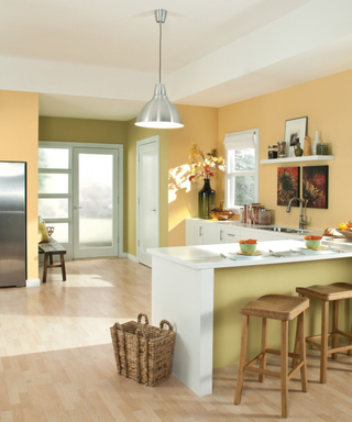 A yellow kitchen with barstools and a door in the background.