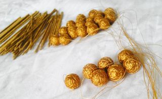A white cloth with balls of woven gold thread and gold sticks next to them in the back