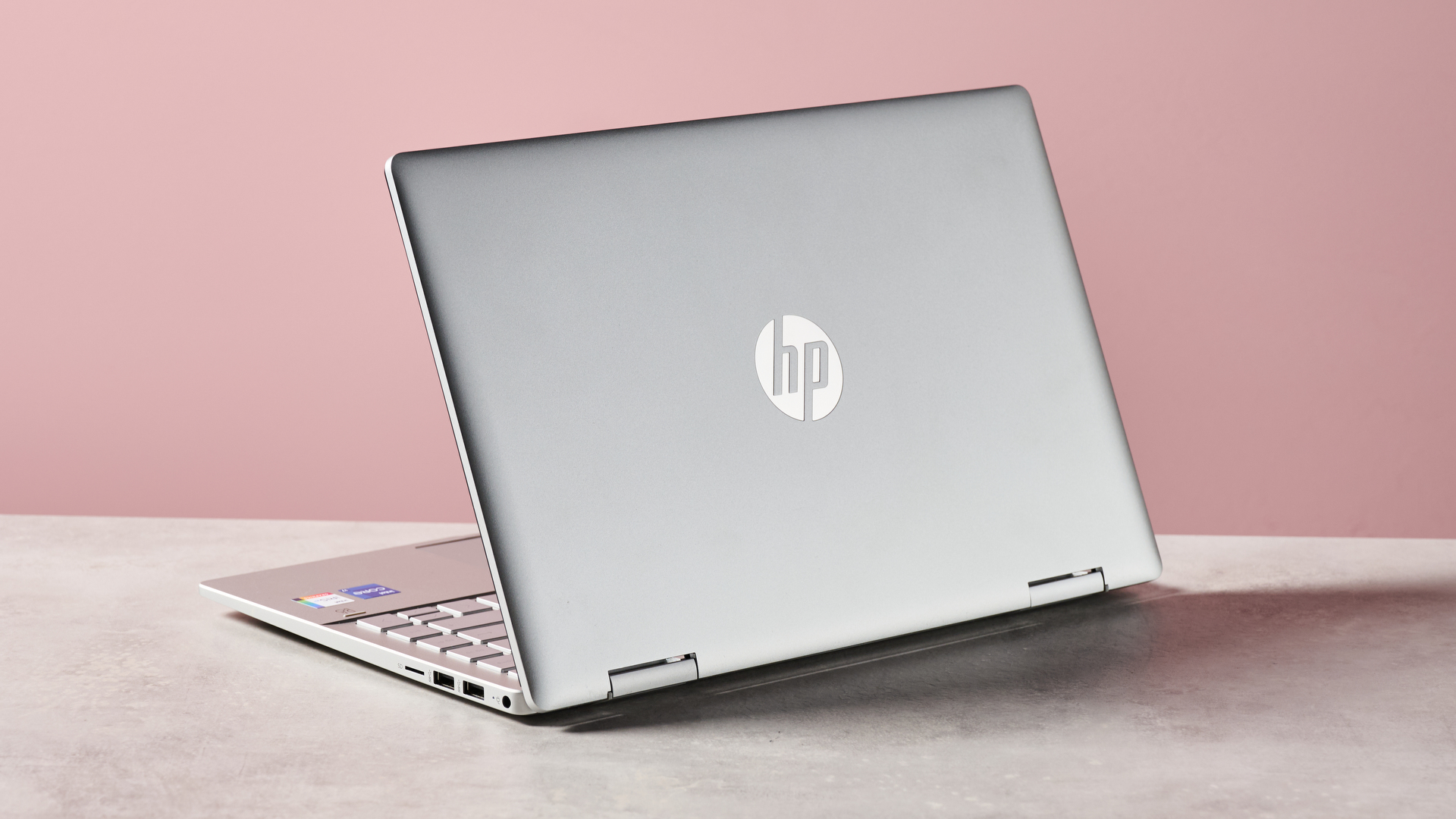 Rear three-quarter view of HP Pavilion x360 14 open on desk with pink wall in background