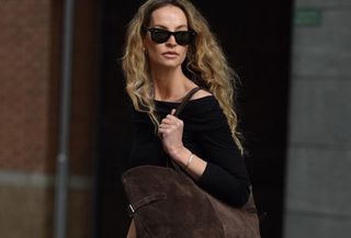 Woman wearing white maxi skirt, black sweater, and large suede tote bag.