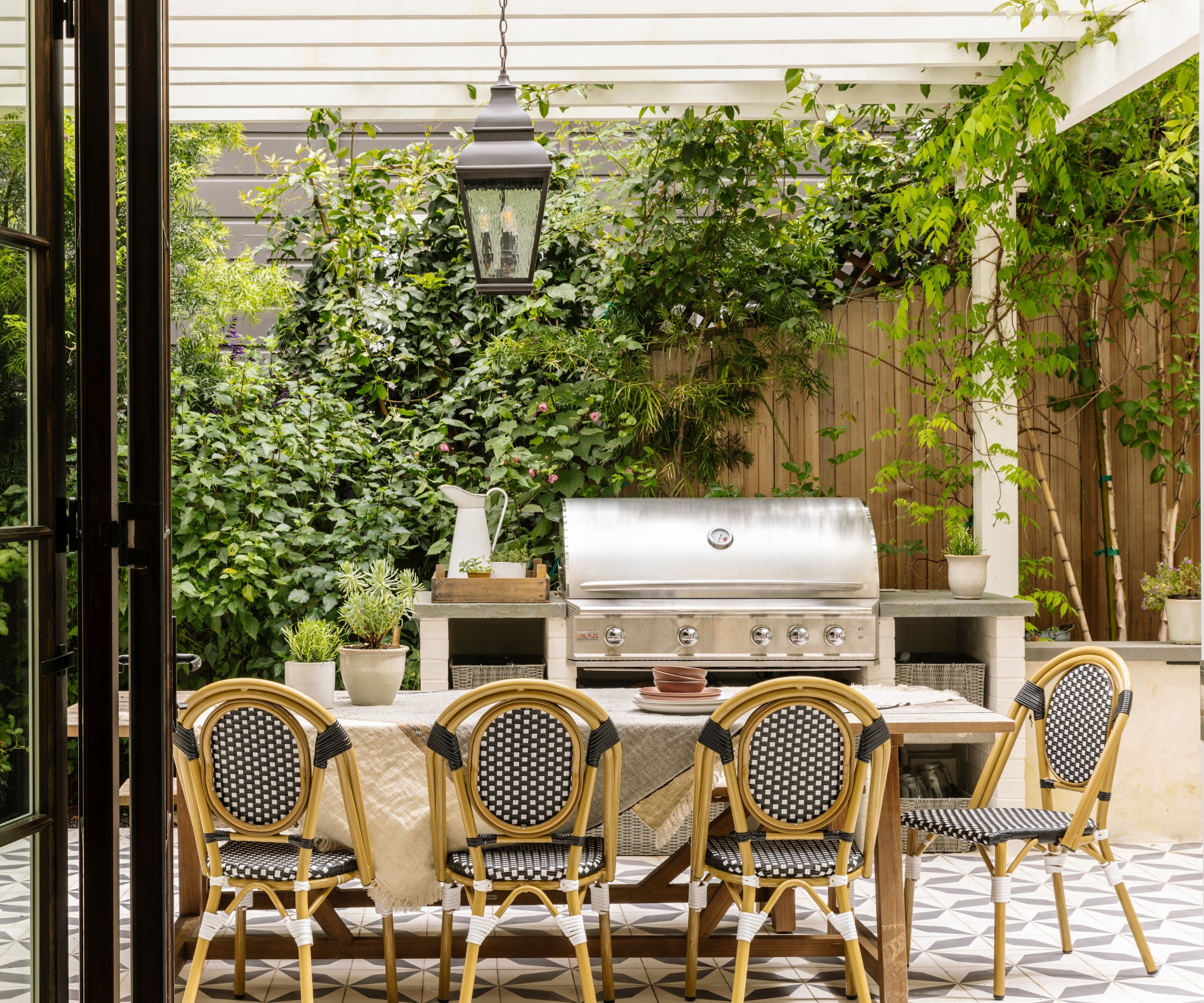 An outdoor kitchen and dining area with a stainless steel stone, patterned floor tiles, and a wooden dining table