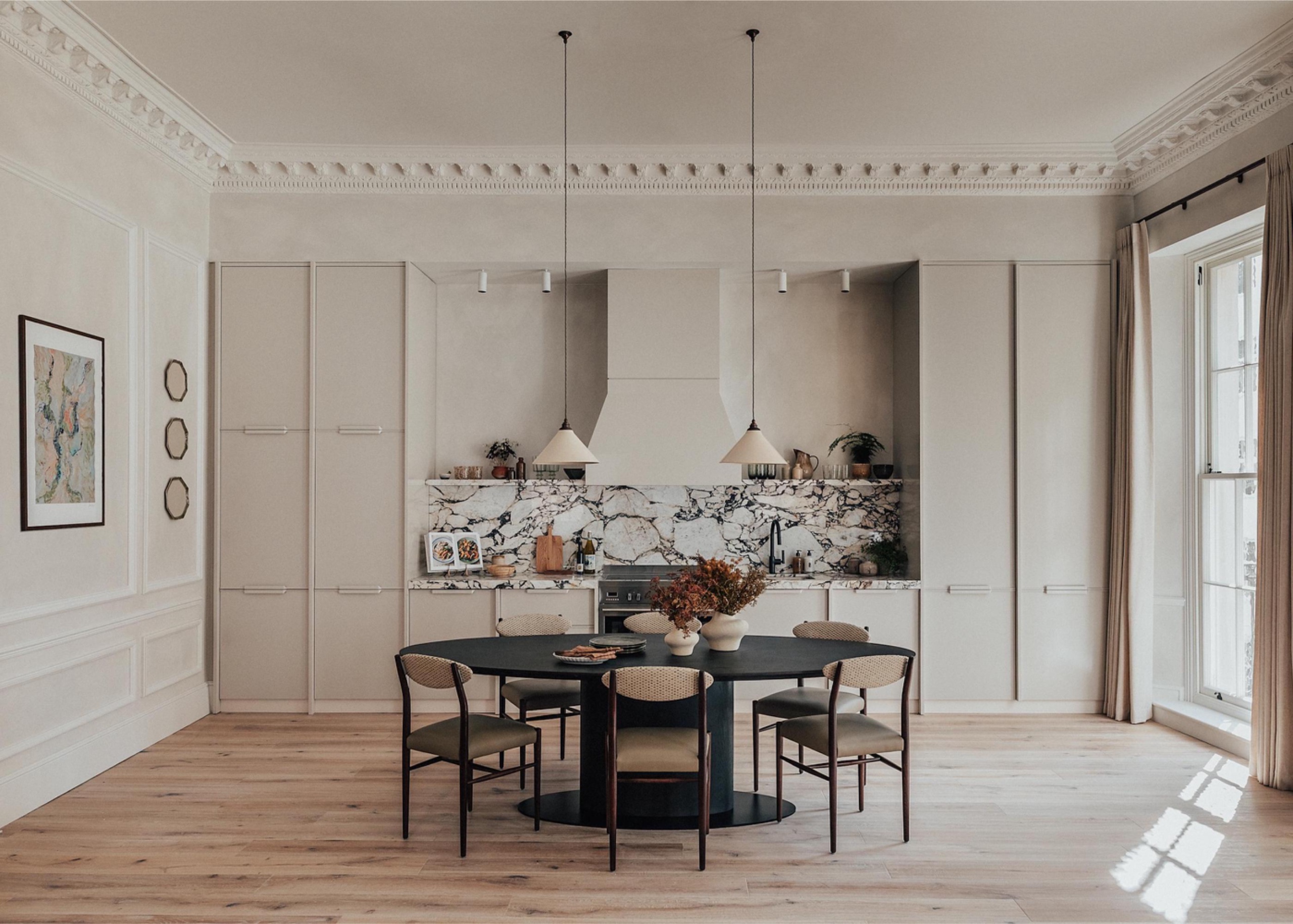 Single-wall kitchen by A.LONDON with veined marble backsplash, open shelving and full-height cabinetry behind a dark wood dining table with sculptural ceramic pendant lights.