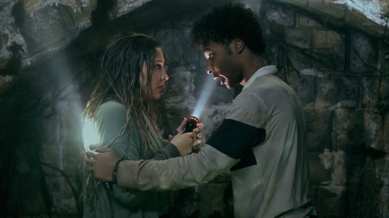 From left to right: Madelyn Cline looks scared while holding a flashlight and Jonathan Daviss holds her arms and a flashlight.