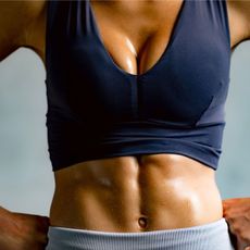 A close up of a woman's abdominal muscles: stood with her hands on her hips doing deep core exercises at the gym