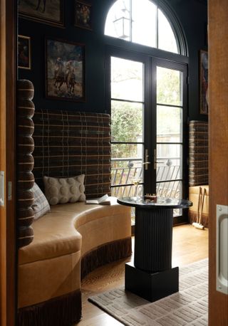 A dining space with curved leather banquette seating, a small bistro style table and dark green-black walls