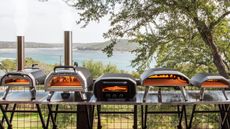 Five Ooni pizza ovens in a row, in front of a bay representing tests to find the best Ooni