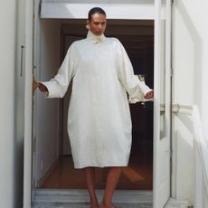 A St. Agni model standing in a doorway wearing a white jacquard coat