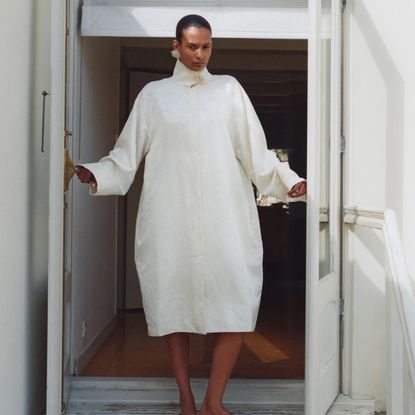 A St. Agni model standing in a doorway wearing a white jacquard coat