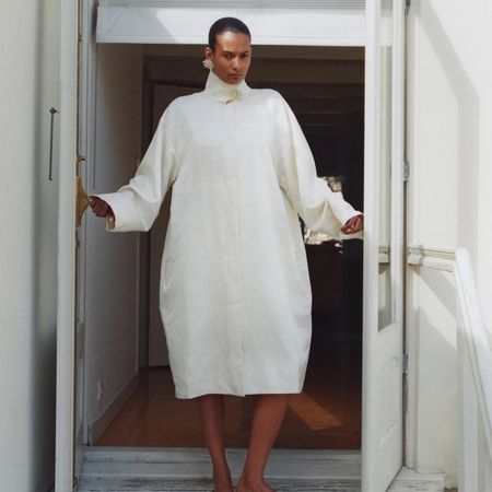 A St. Agni model standing in a doorway wearing a white jacquard coat