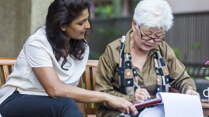 A young woman sit together on a park bench while the older woman signs some paperwork.