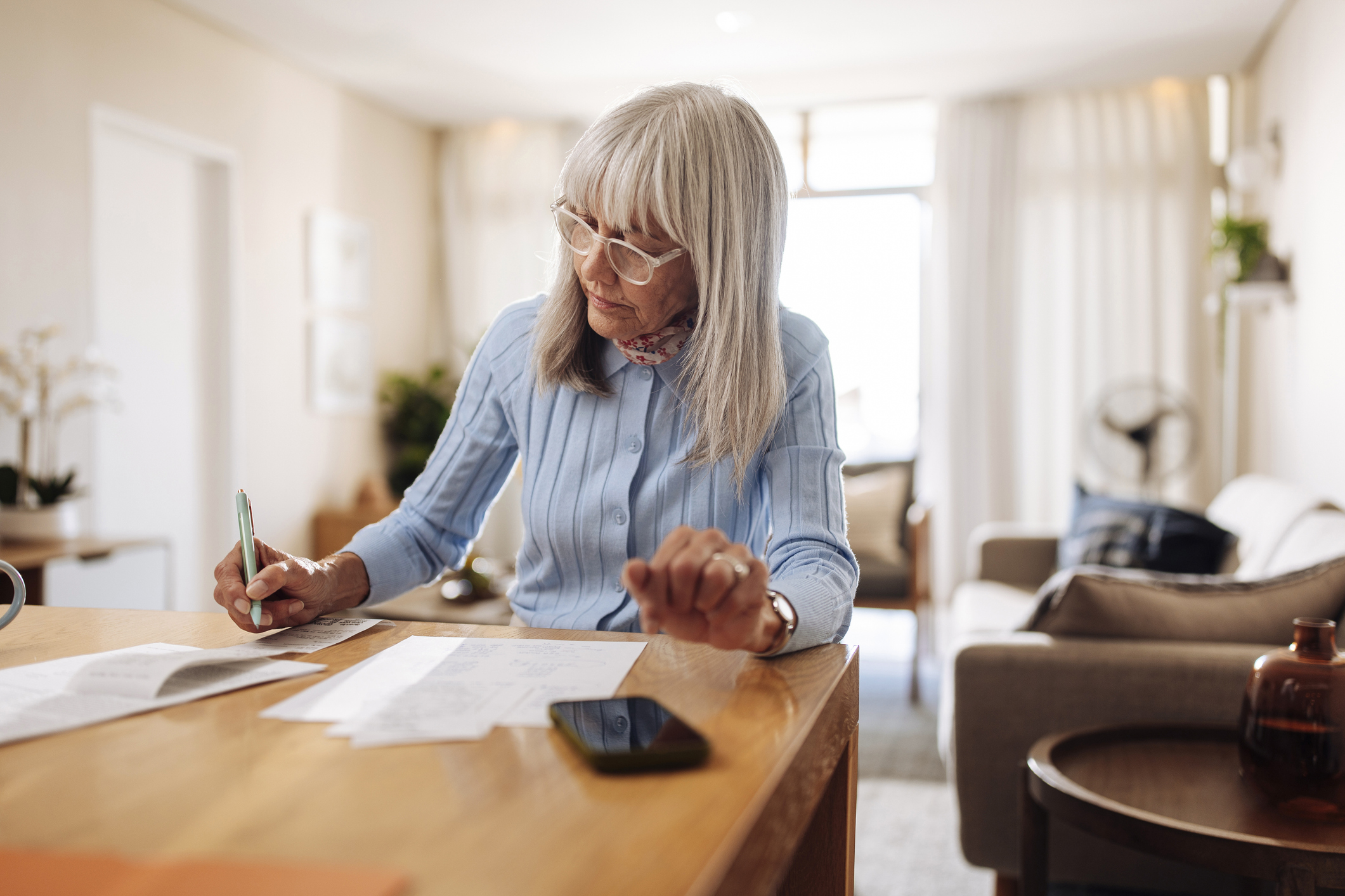 Elderly woman sitting at a kitchen table, reviewing bills and budgeting documents
