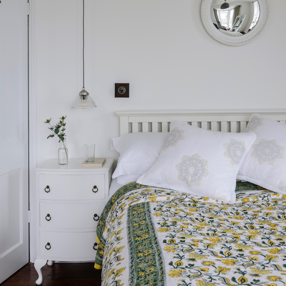 White bedroom with double bed, floral duvet and pendant light hanging over side table