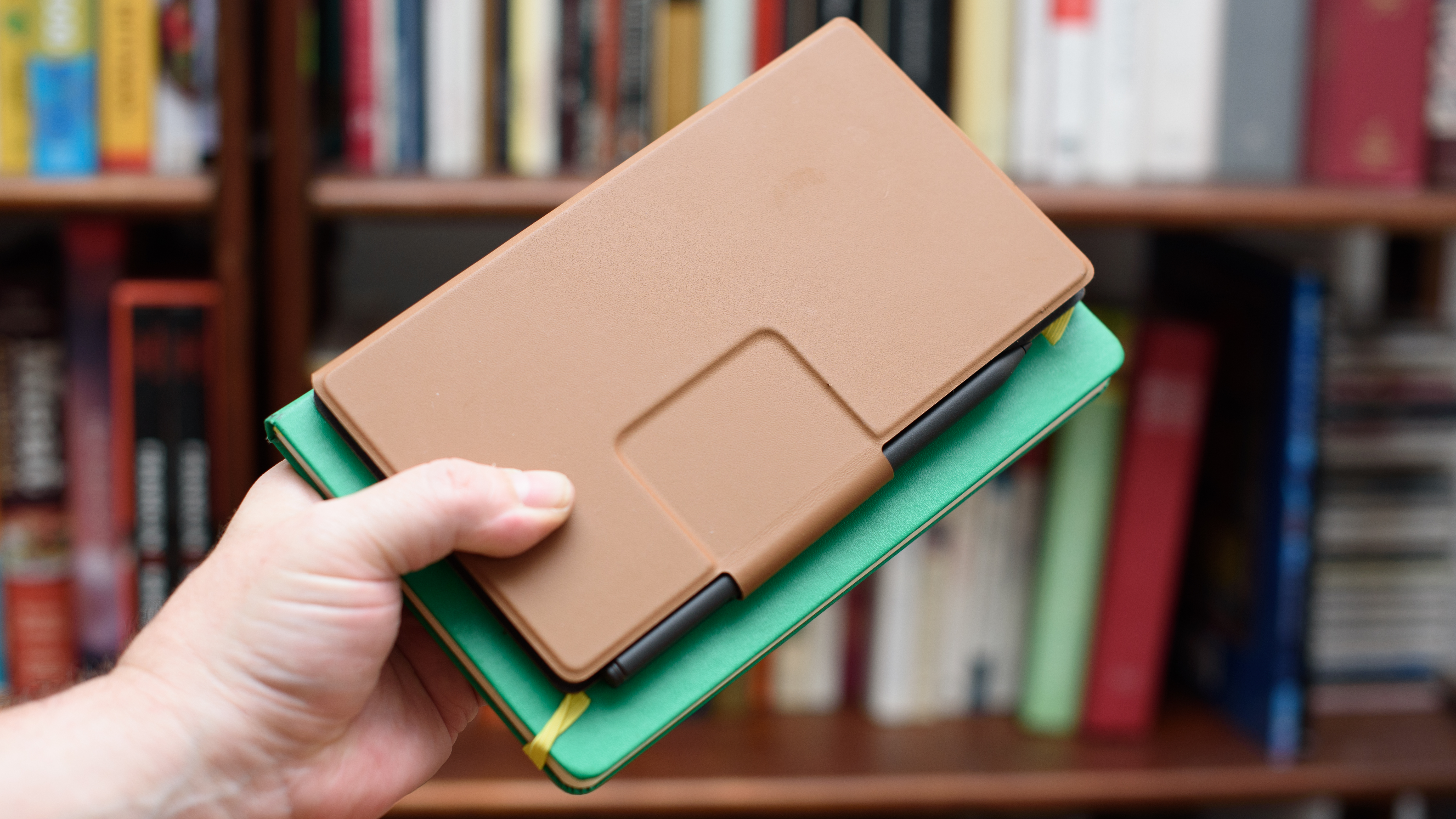 reMarkable Paper Pro Move tablet in front of a library of books, showing various writing screens and comparing the size to a Moleskine notebook