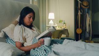 A woman reading in bed while drinking from a mug