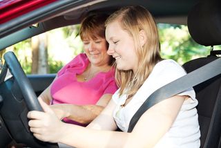 A mom gives her teen daughter a driving lesson.