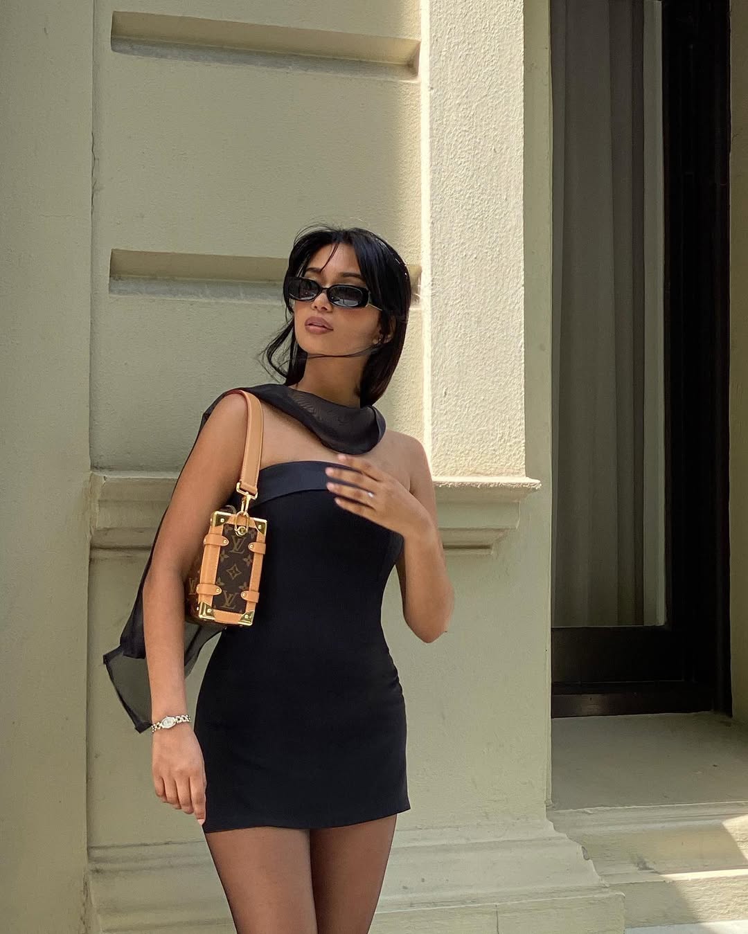 An image showing @mishti.rahman posing outside, wearing a black dress and a Louis Vuitton handbag