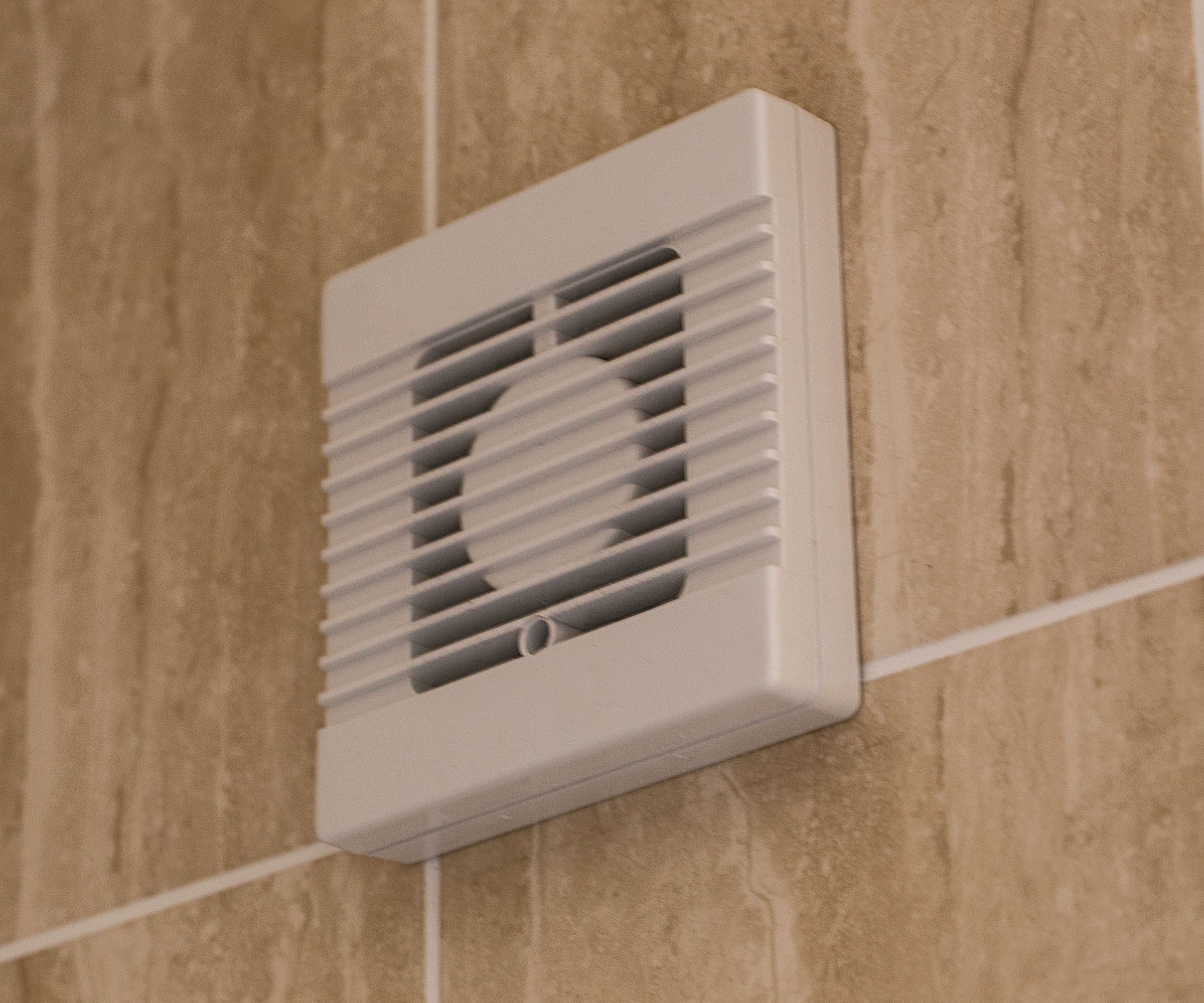 white bathroom extractor fan on beige wall tiles