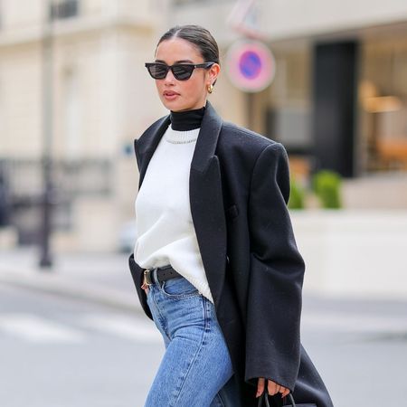 sunday riley luna sleeping night oil - woman wearing sunglasses walks down the street in navy wool coat, white jumper and jeans