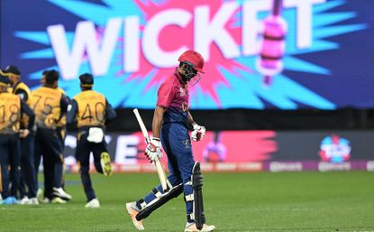 Dismissed batsman walks off in T20 World Cup in front of large screen showing the word 'Wicket' in huge letters