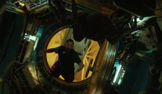 a bearded man floating in a space station looks shocked as he sees a giant spider in a cramped chamber