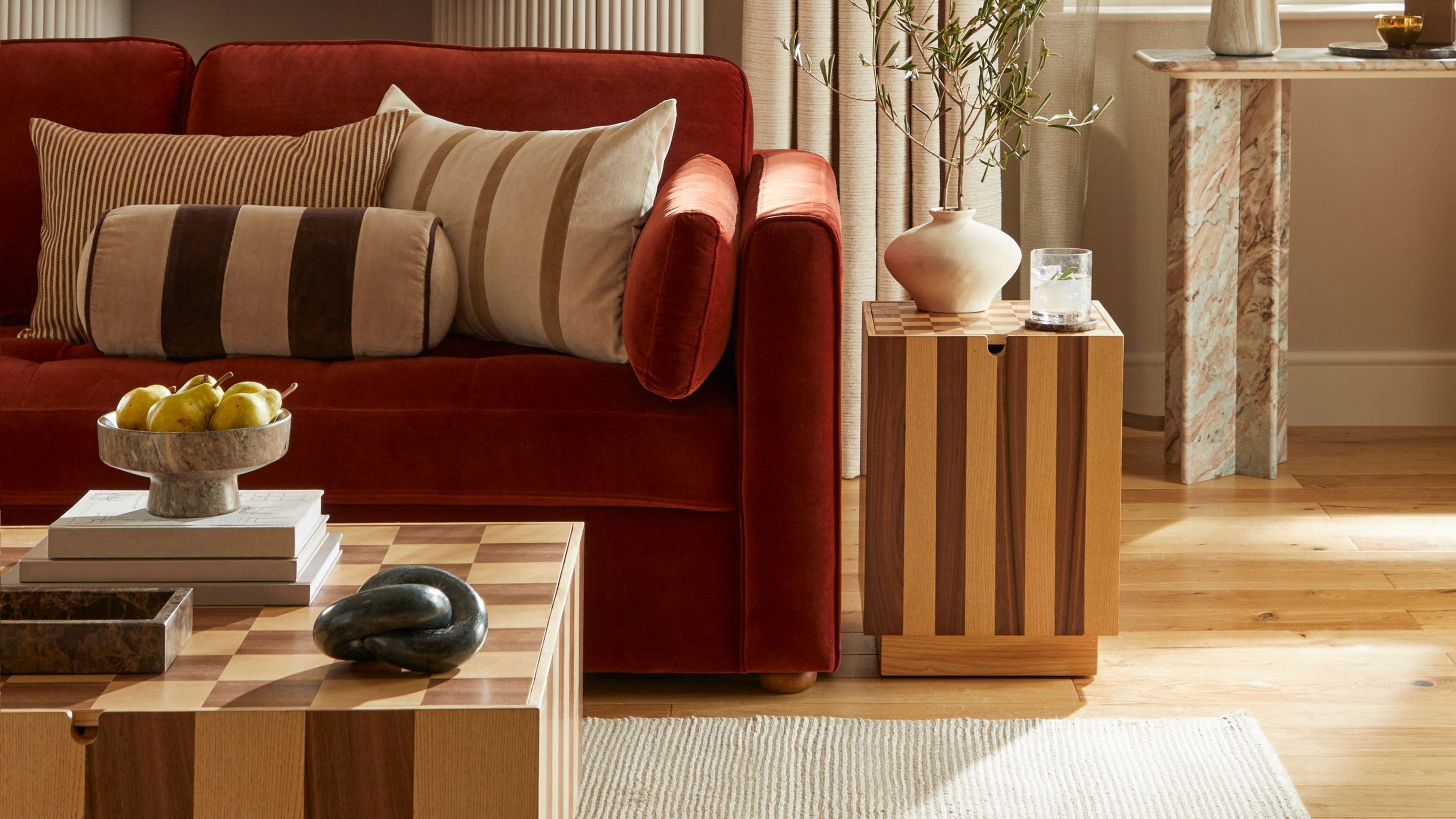 A living room with a rust red velvet sofa and the chequerboard Dunelm Harmon side table next to it and the matching coffee table in front of it
